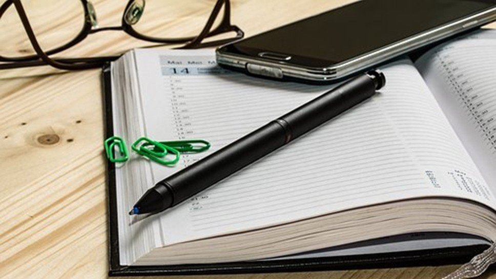 Otwarty terminarz z długopisem i telefonem, leżące na biurku.